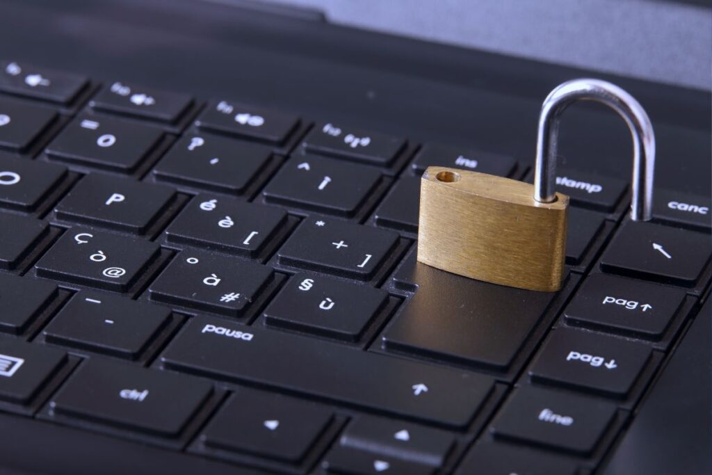 Um cadeado de latão aberto posicionado sobre a tecla "Enter" de um teclado de laptop escuro, sugerindo segurança.