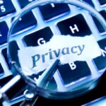 Uma lupa amplificando a palavra "Privacy" escrita em um pedaço de papel sobre um teclado de laptop.